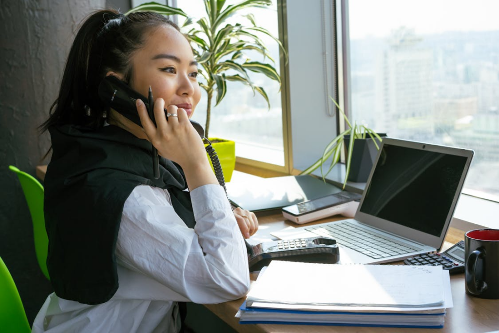 image of a woman sitting on her chair while answering a call in front of her laptop